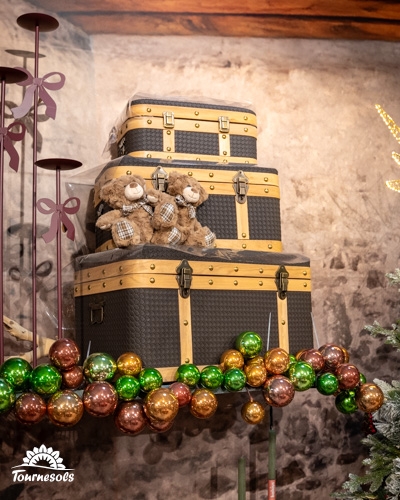 Empilade de valises vintage avec ours en peluche, ornée de boules de Noël colorées.